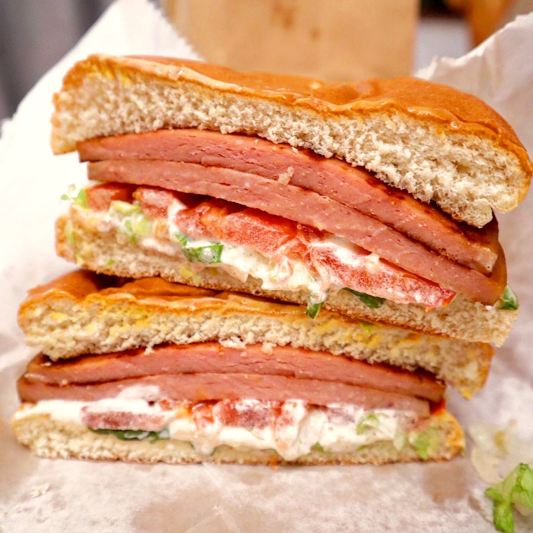 A bologna, mayo, lettuce and tomato sandwich cut in half and stacked