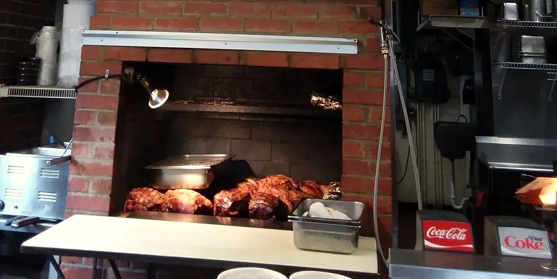 The brick pit behind the counter at The Pit, loaded with meat under a heat lamp