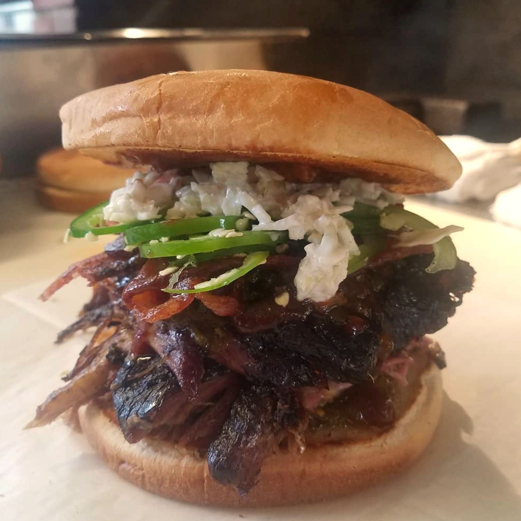 A barbecue sandwich piled high with jalapeño slices and slaw on a toasted bun, from The Pit's Instagram
